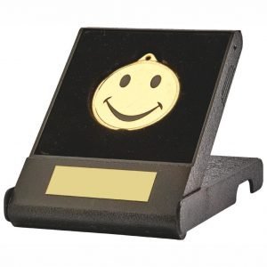 Black coloured moulded plastic open and shut flip box with a standard 45mm dia printed happy face medal sits in a black coloured recessed liner